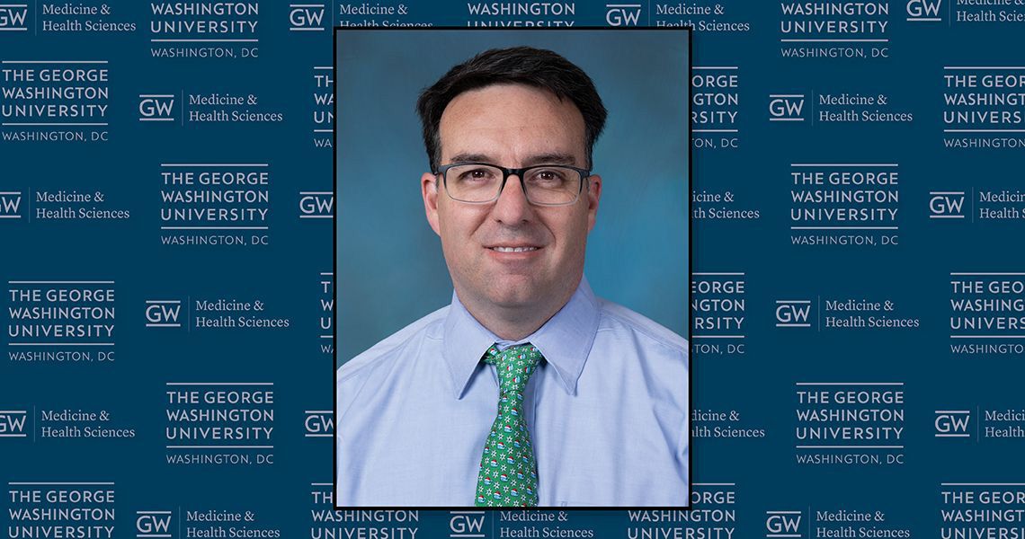 Scott Krugman in front of a GW logo background